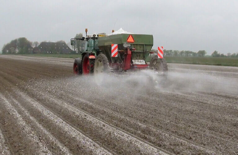 Landbouwgips met trekker over akker strooien